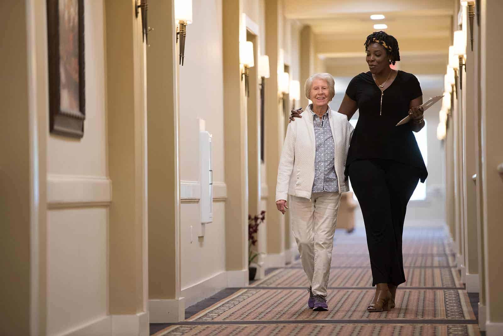 Senior woman and staff member walking down hallway